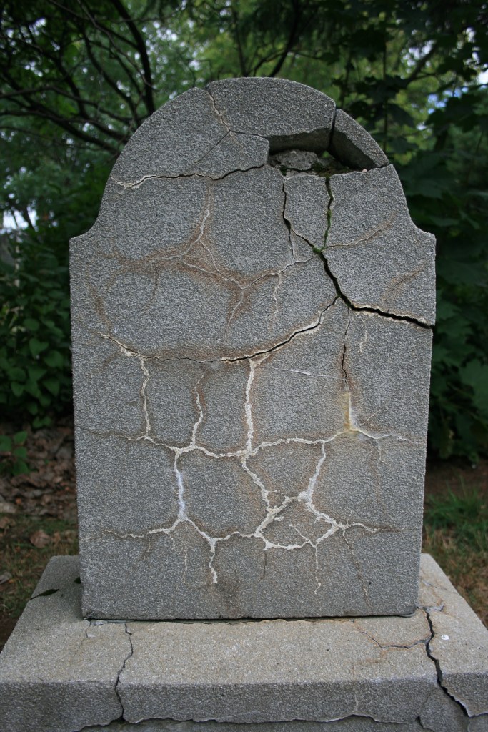 A grey tombstone with no writing on it. It is covered in thin cracks.